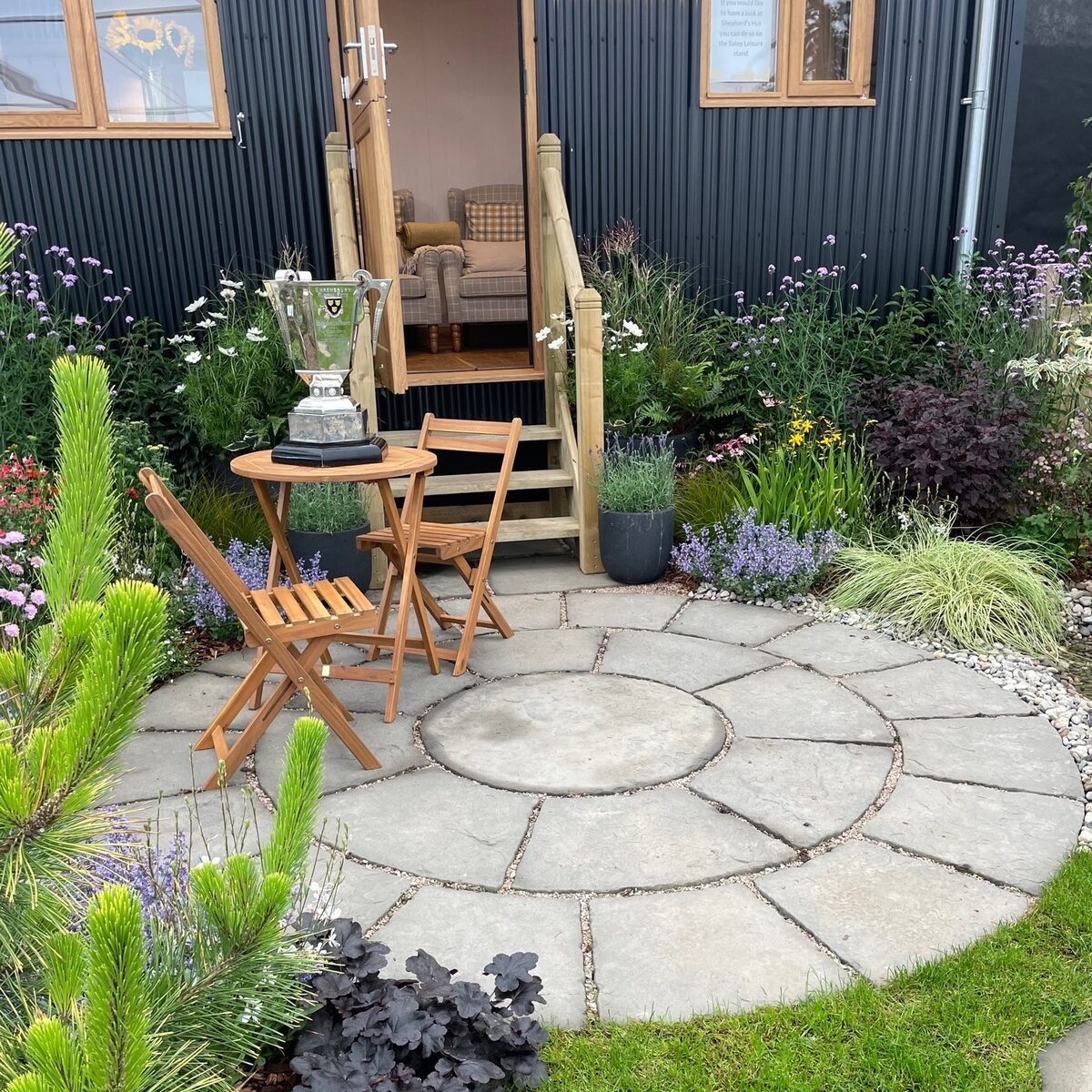 stone patio circle with table and cahirs outside black shepherds hut.