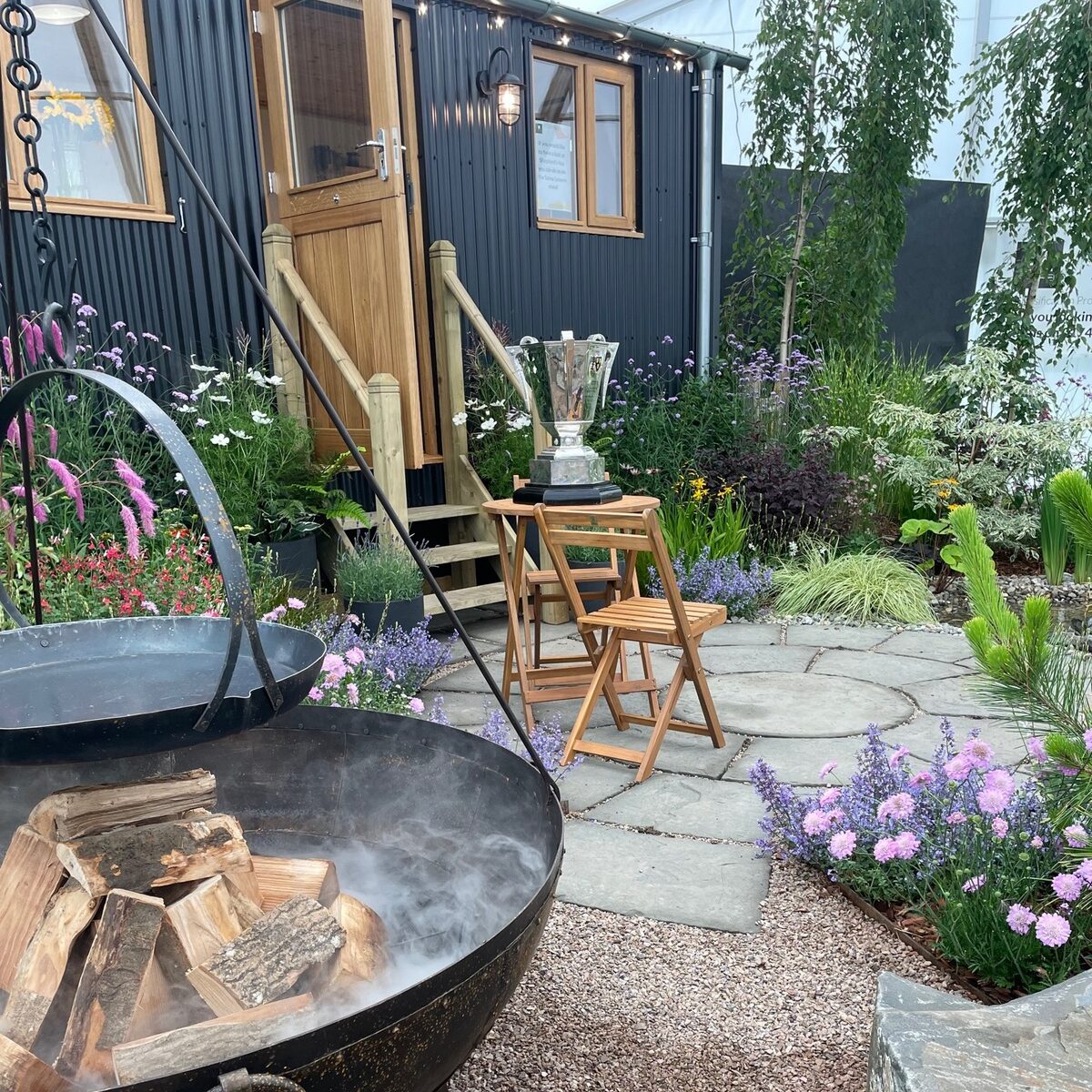 stone patio outside black shepherds hut with fire pit left.
