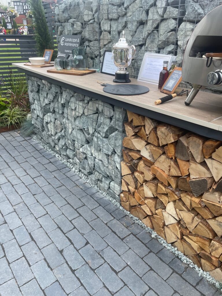 grey cobble patio with outdoor kitchen to the right a mix of wood and stone underneth the counter